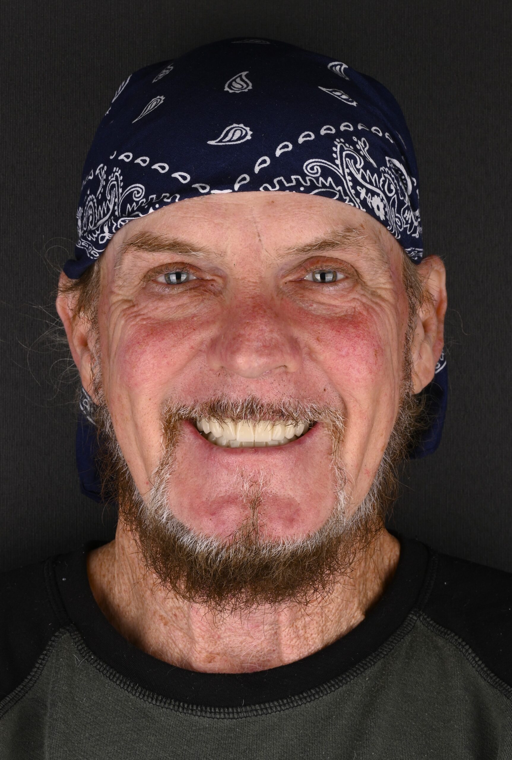 Smiling man wearing a dark bandana with white paisley patterns, close-up portrait.
